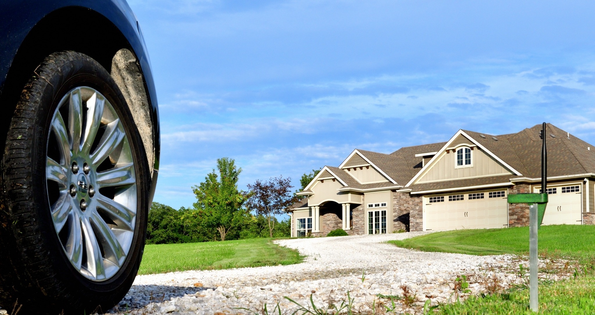 Driveway Sensor installed on a stake beside a driveway with a vehicle and house
